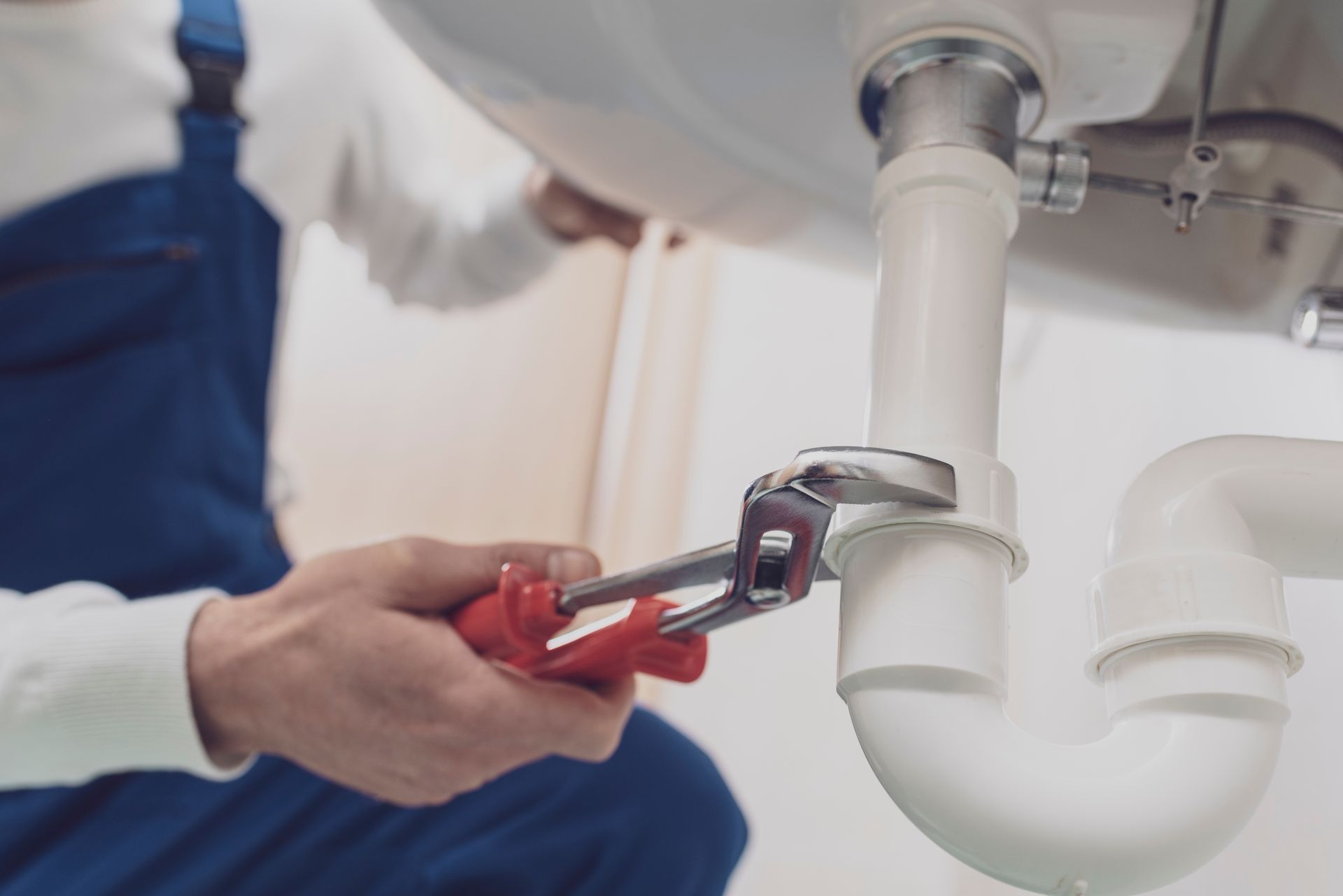 A plumber is tightening a P-trap under a sink with a wrench during a plumbing repair.