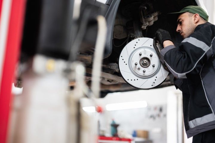 A man is fixing a brake disc on a car in a garage.