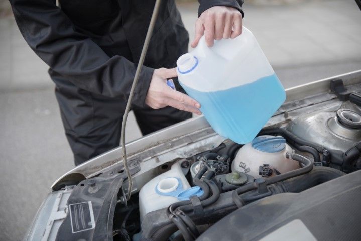 A person is pouring windshield washer fluid into a car.