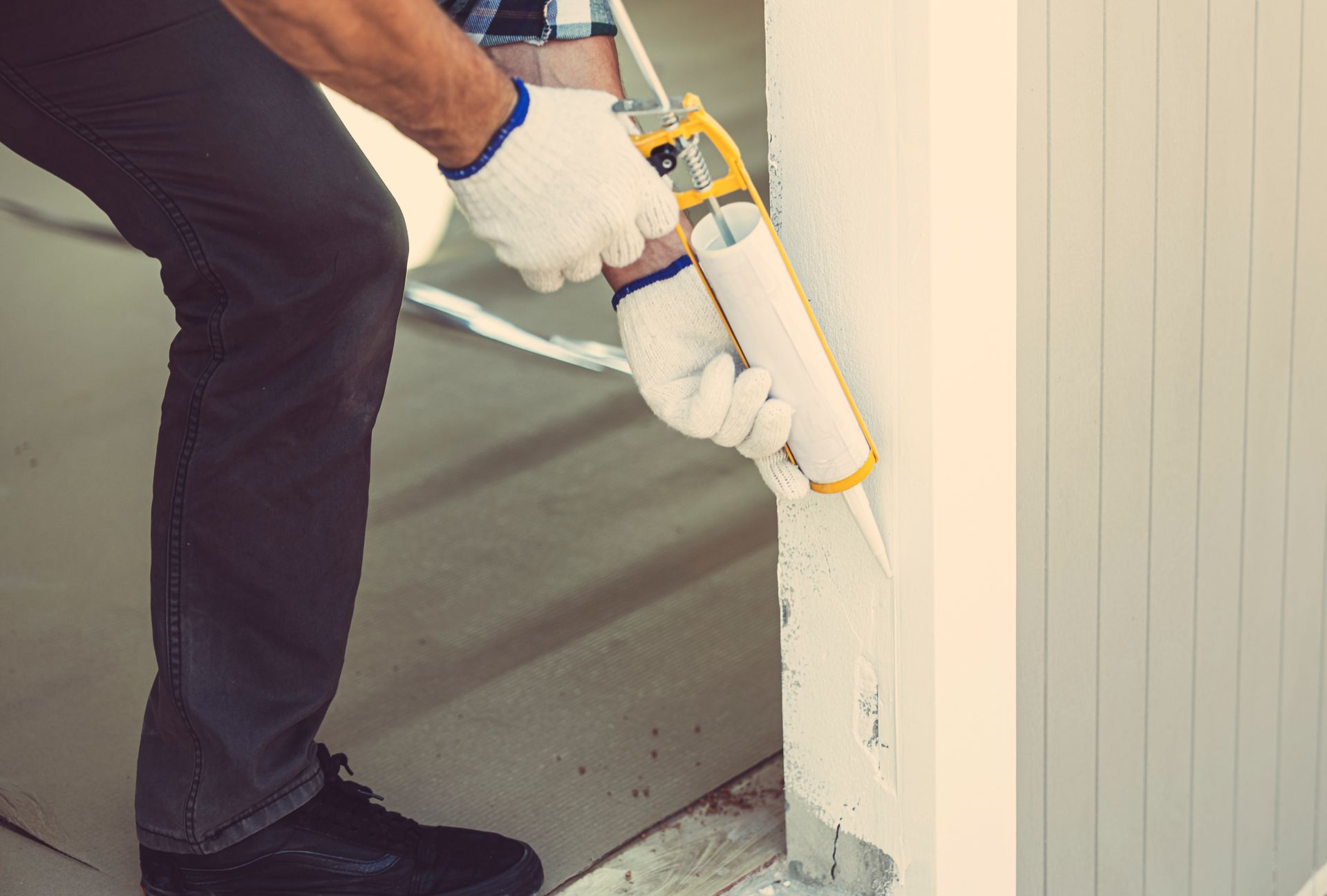 A man is applying silicone sealant to a wall.