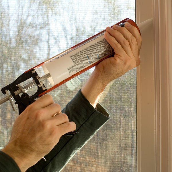 A person is applying silicone to edge of window