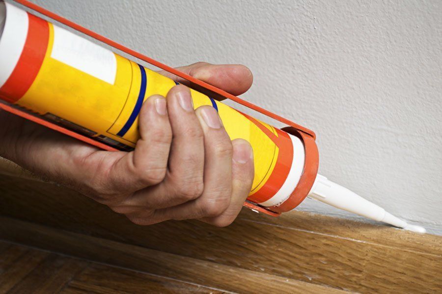 A person is applying caulk to a wooden floor.