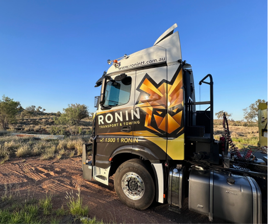 Orange excavator in a dirt lot, arm extended, near piles of gravel.