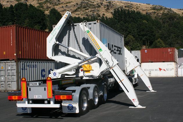 Green tractor on a flatbed trailer, being transported on a rural road.