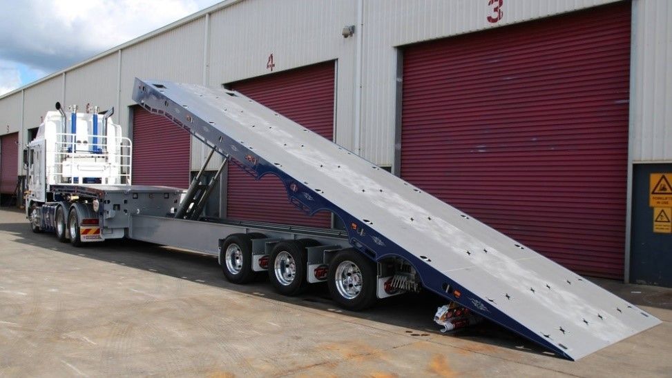 Semi-truck and trailer with extended ramp. Gray ramp against maroon loading dock doors.