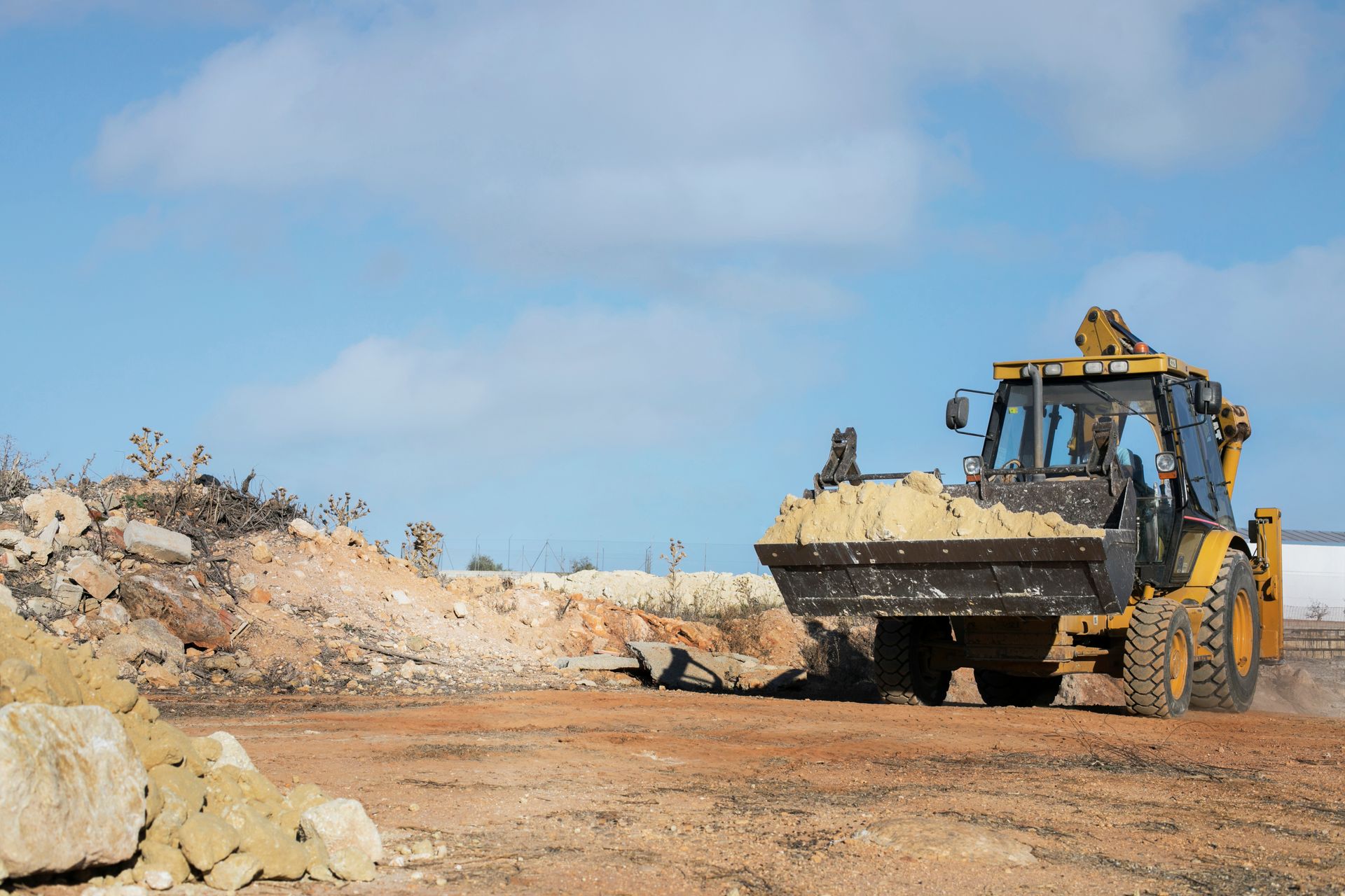 Yellow backhoe moving dirt on a construction site under a blue sky.
