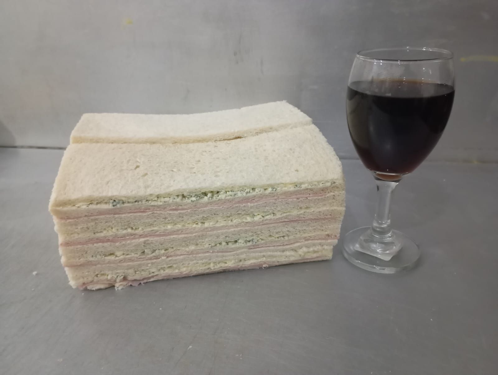 Pila de sándwiches y una copa de vino tinto en un mostrador.