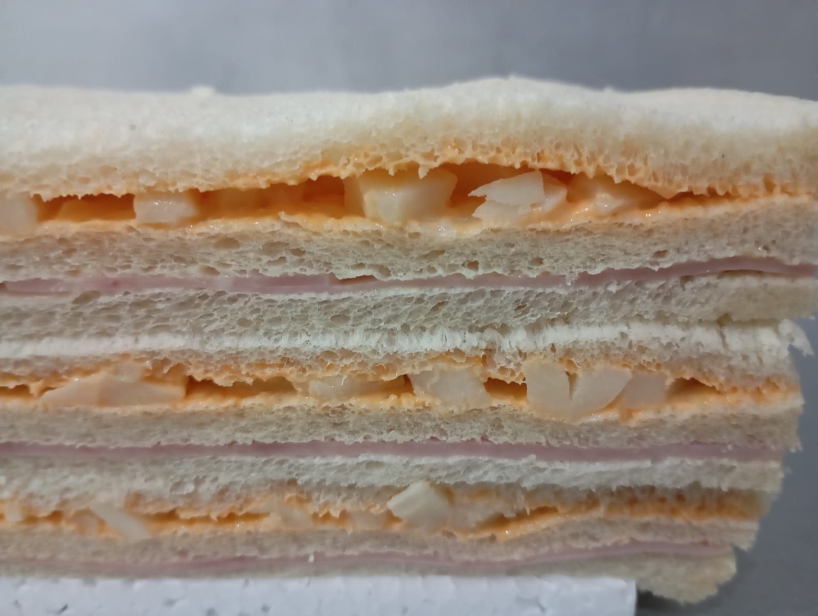 Sándwich cortado por la mitad, apilado. Capas de jamón, ensalada de huevo y pan.