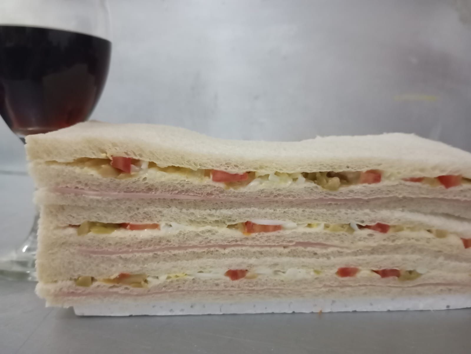 Sándwich apilado con jamón, tomate y una copa de vino tinto.