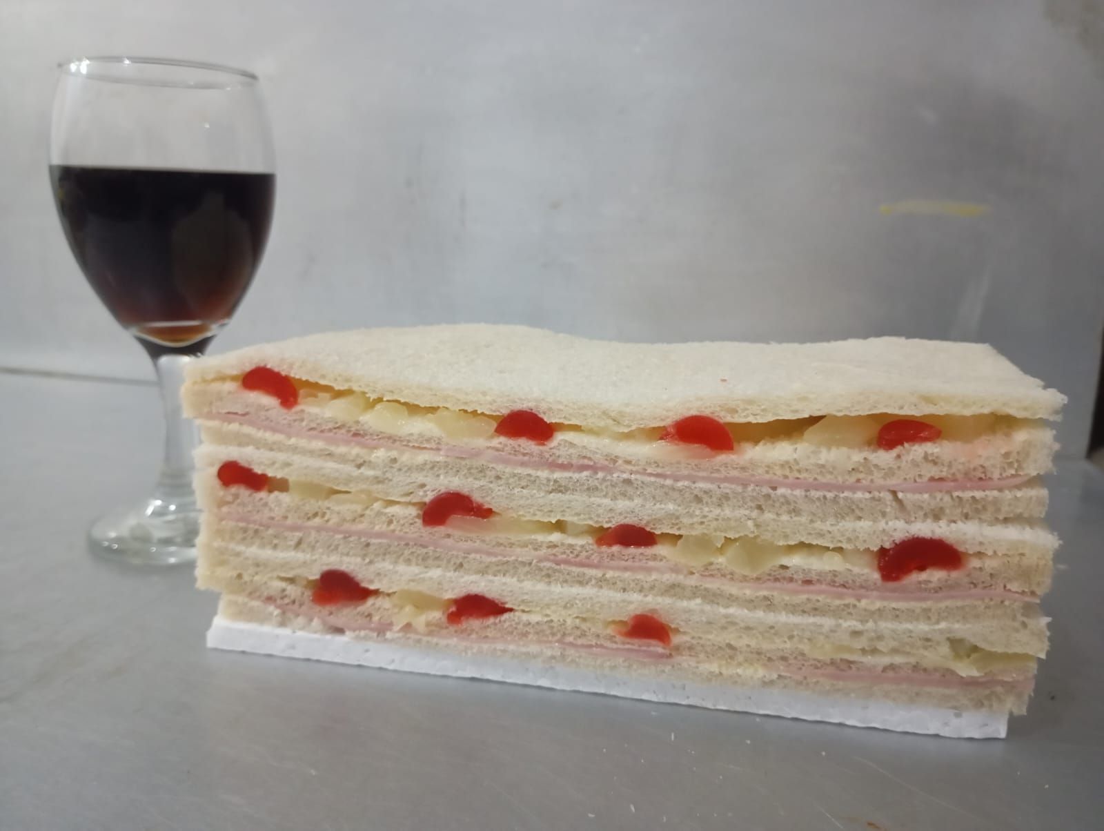 Sándwich de capas con cerezas y un vaso de líquido oscuro.