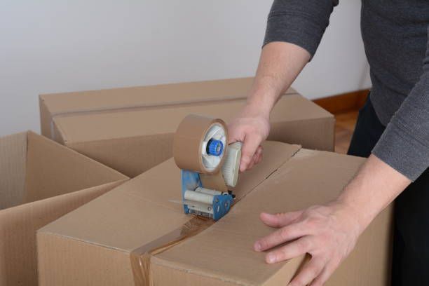 Person sealing cardboard box with packing tape, indoor setting.