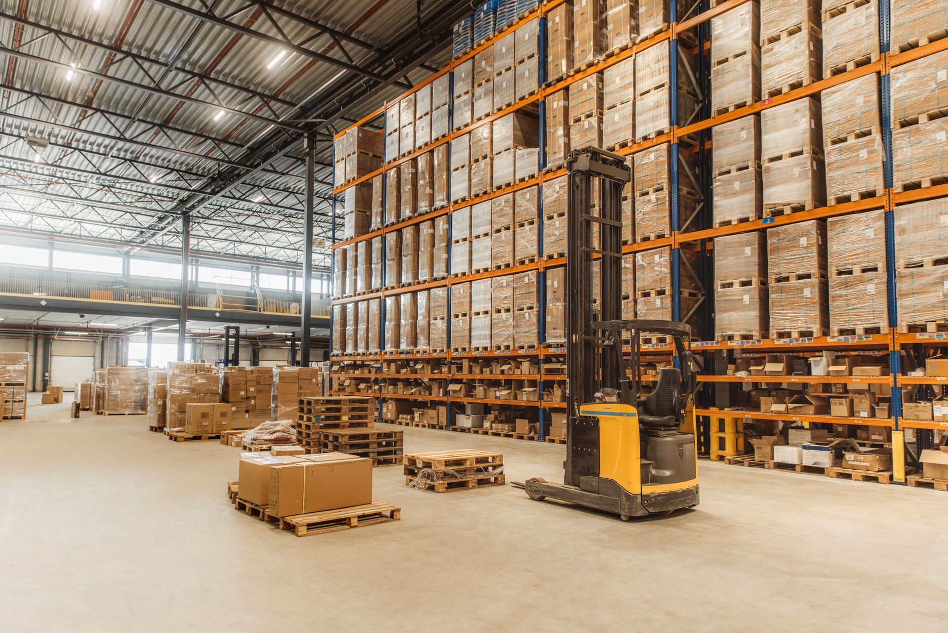 Forklift in large warehouse storage facility with stacked pallets and high industrial shelving.
