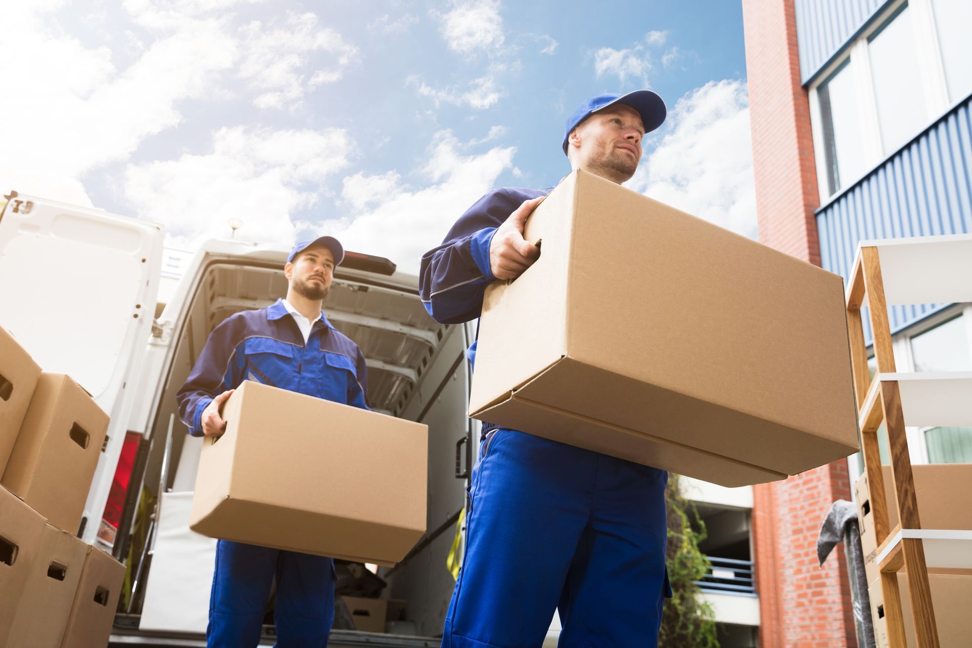 Residential movers from Christofferson Moving & Storage in blue uniforms carrying a cardboard box fo