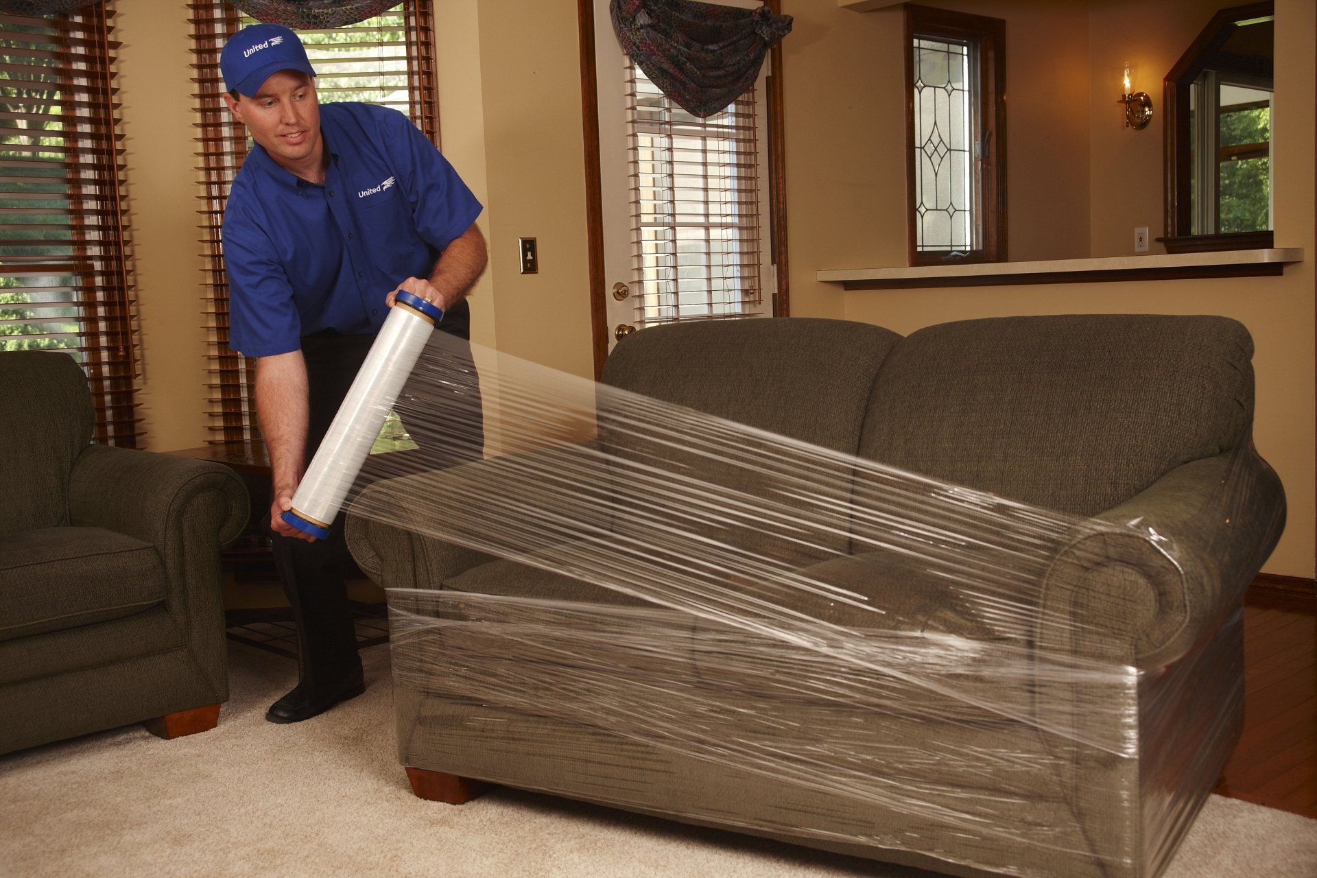 A man wrapping a couch with plastic wrap in a living room