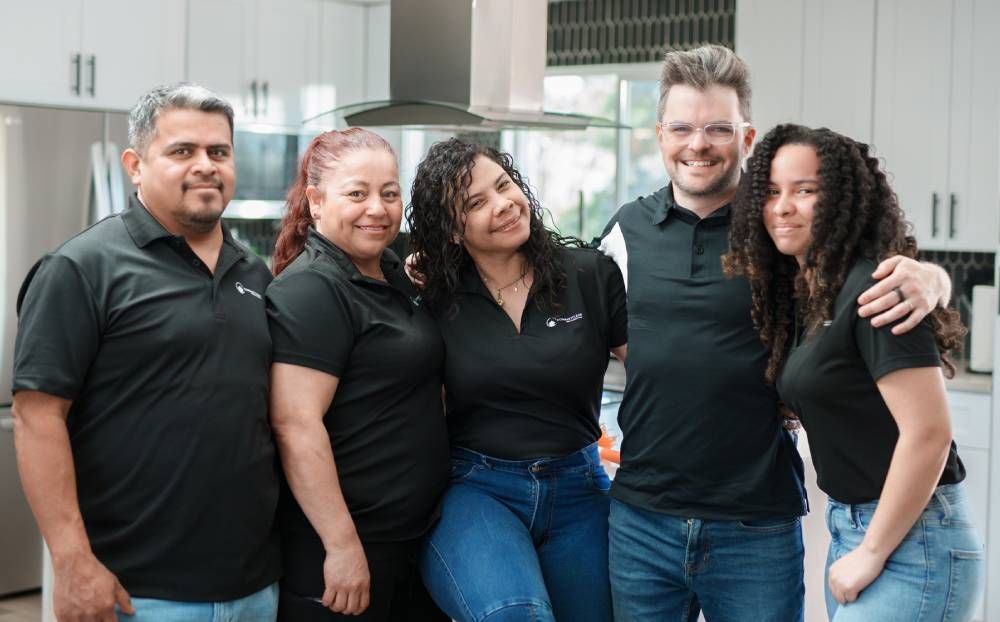 Group of five people, smiling, posing in a kitchen, all wearing black shirts, and jeans.