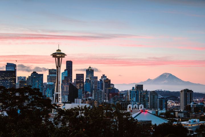 A city skyline with a mountain in the background at sunset.