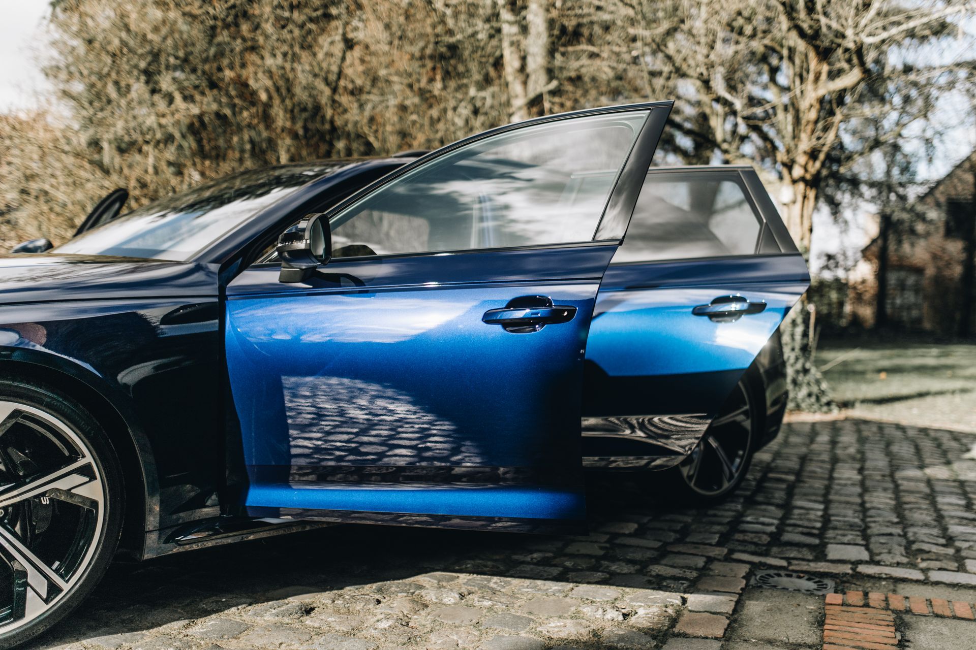 A blue car is parked on a brick driveway with its doors open.