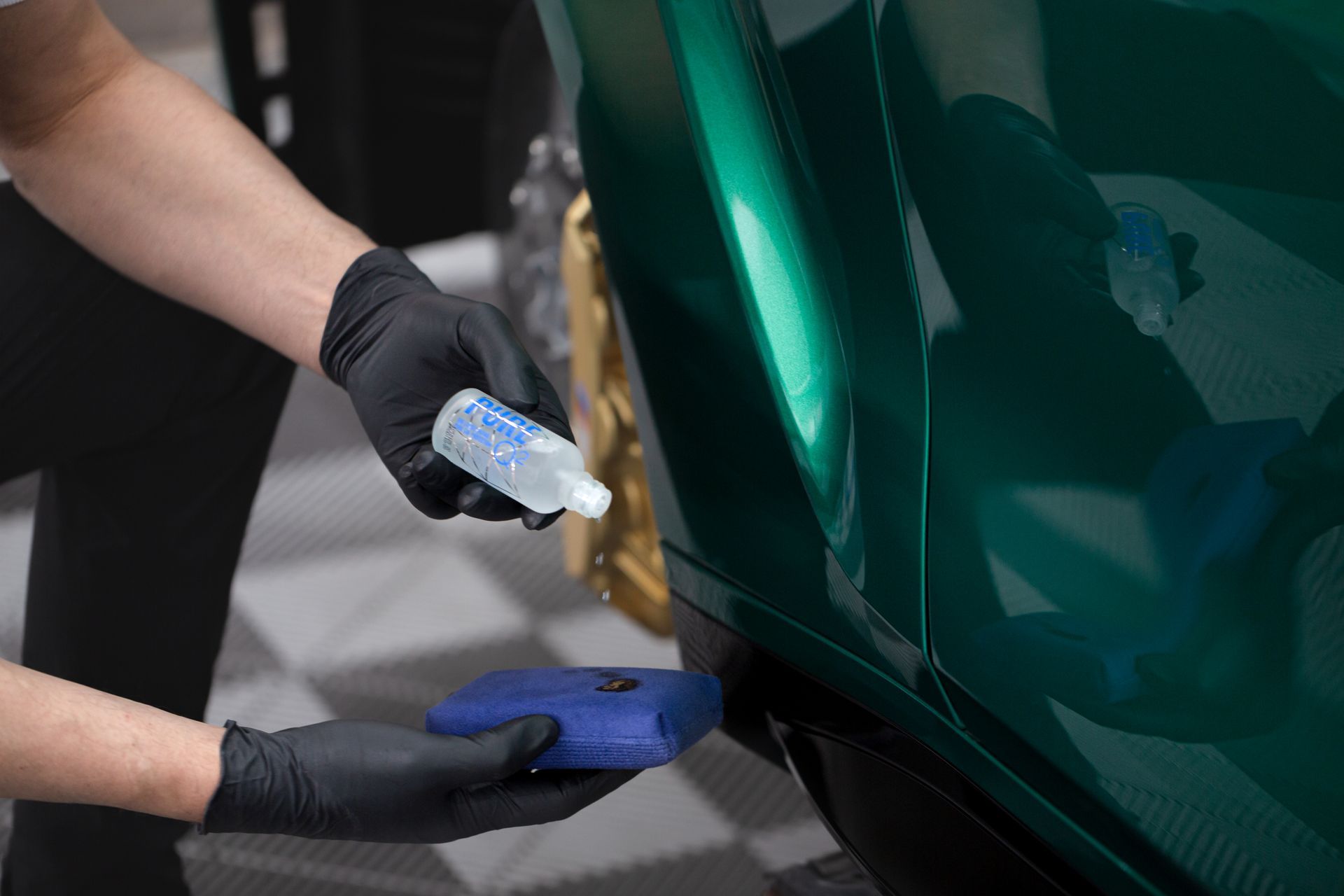 A person is applying a coating to a green car.