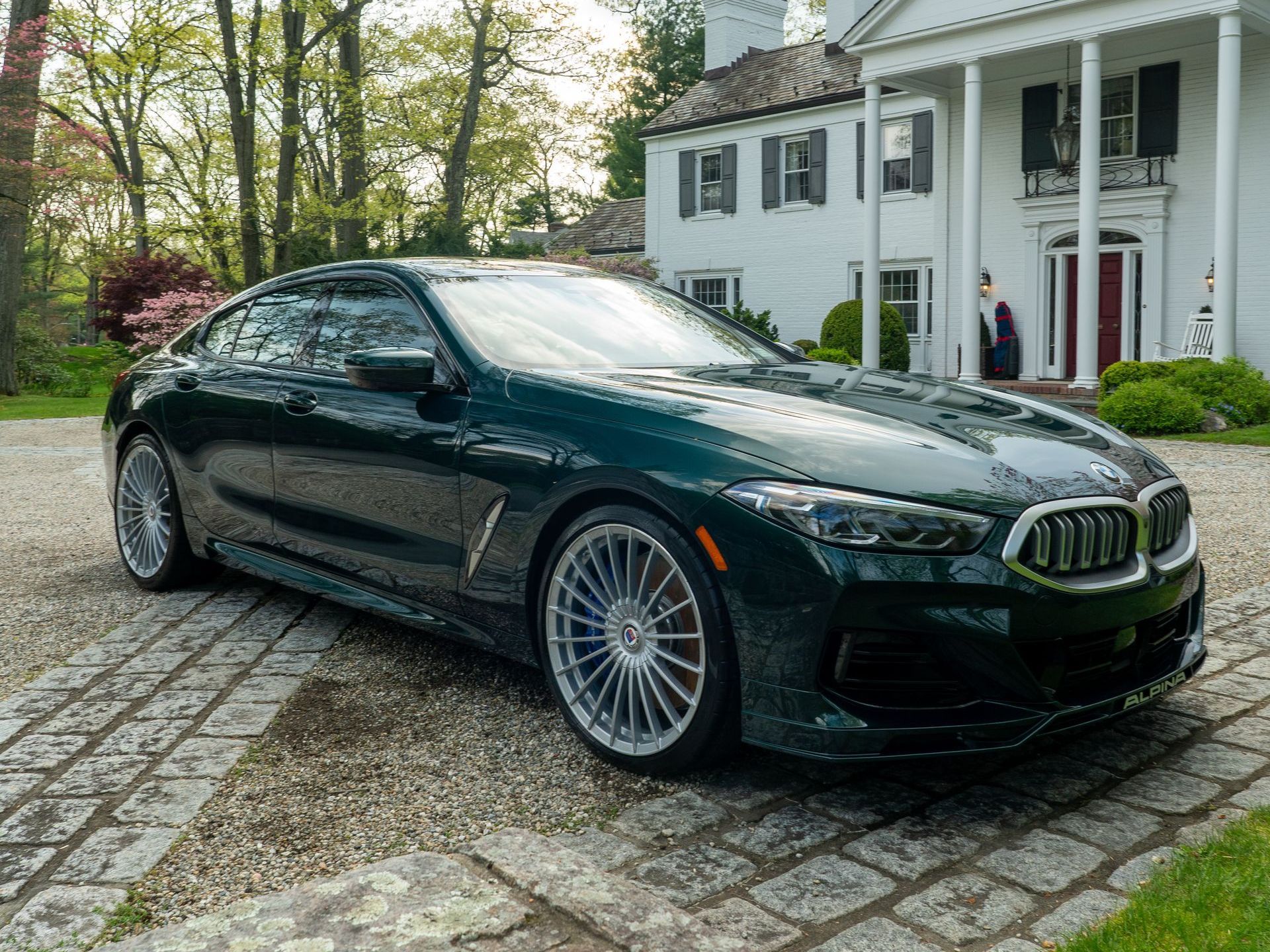 A green bmw alpina b8 coupe is parked in front of a white house.