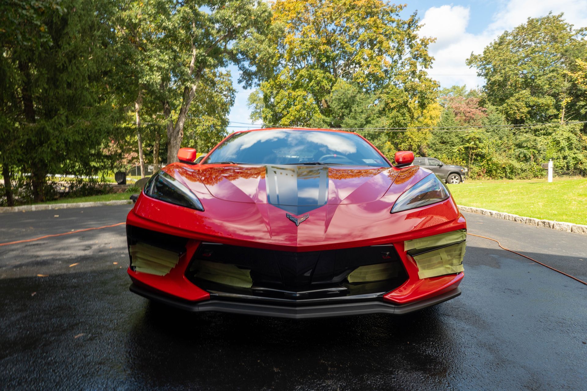 A red sports car is parked in a driveway with trees in the background.