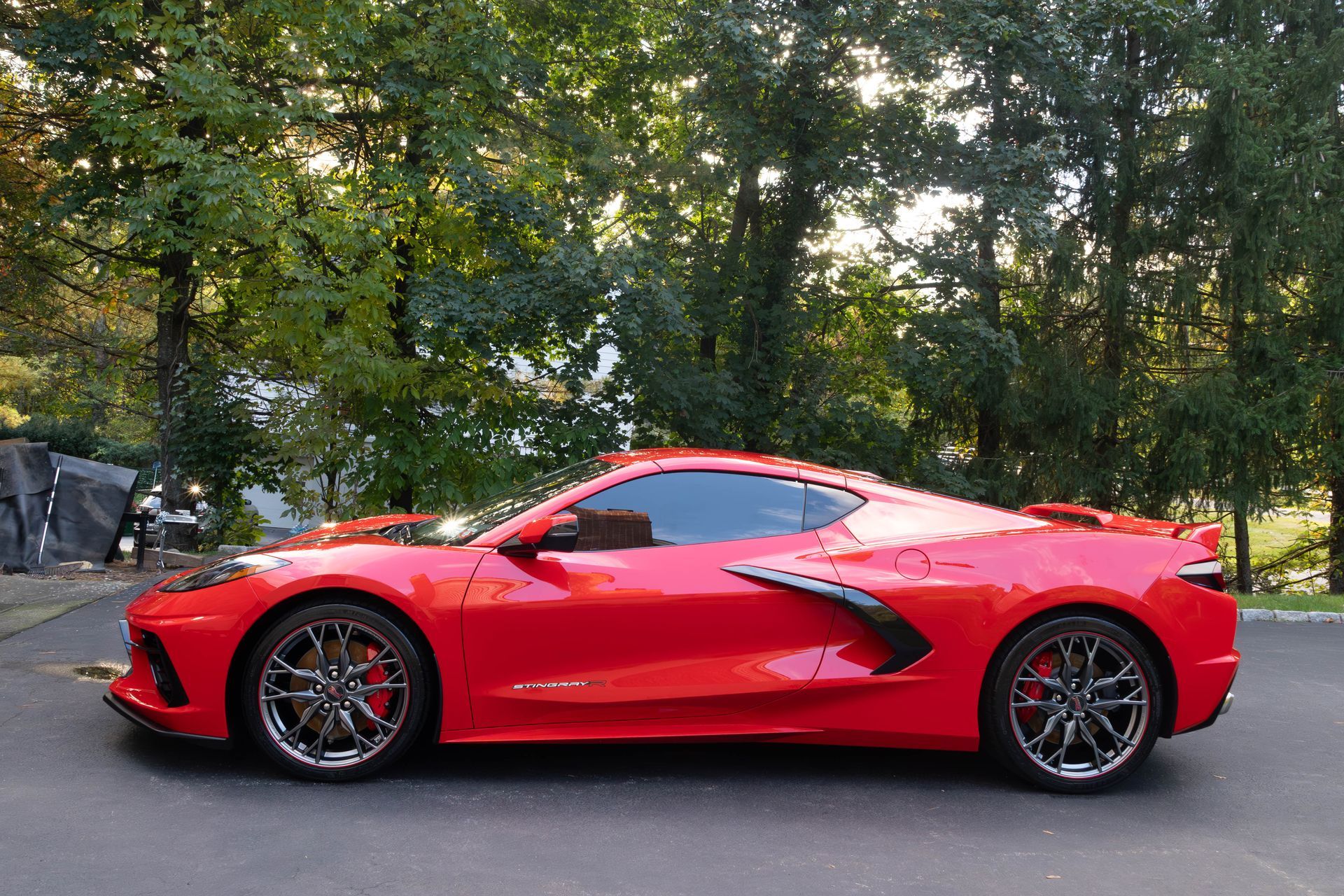 A red sports car is parked on the side of the road in front of trees.