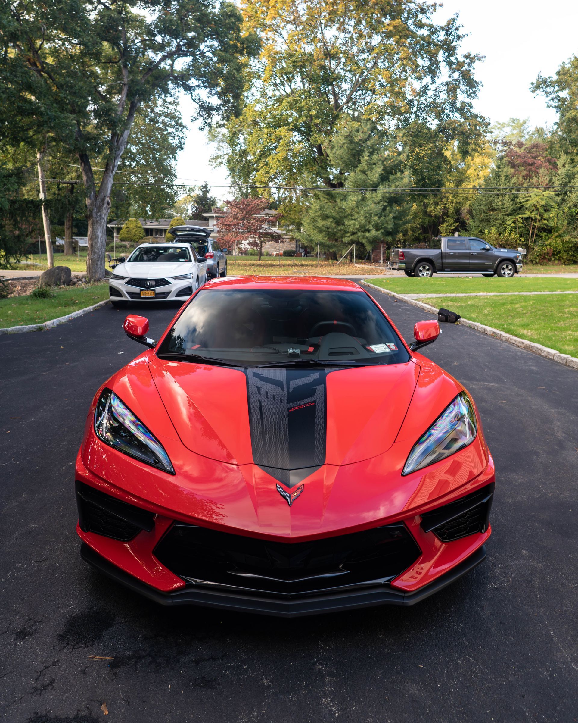 A red corvette is parked in a driveway next to a white car.