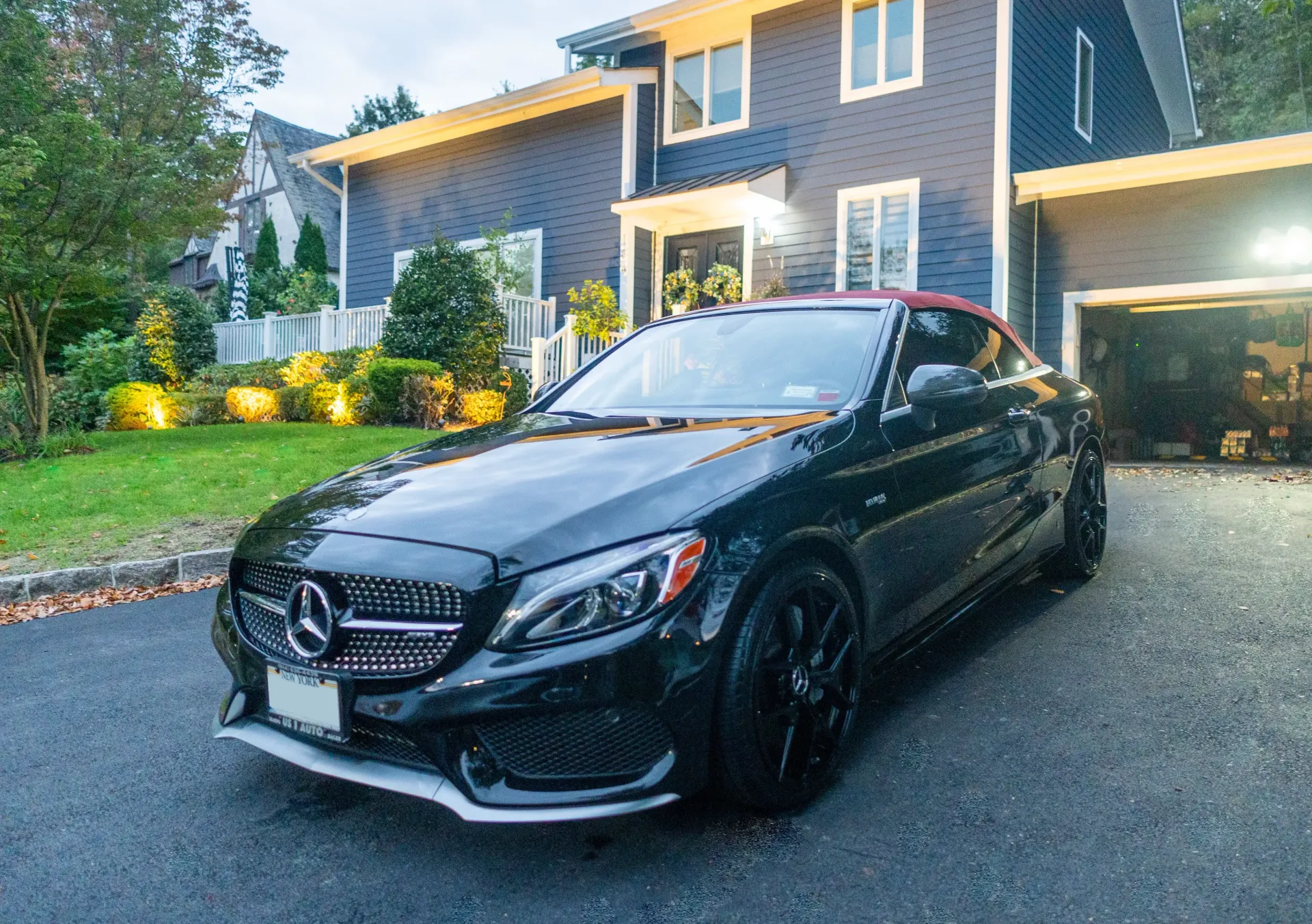 a black mercedes convertible is parked in front of a blue house .