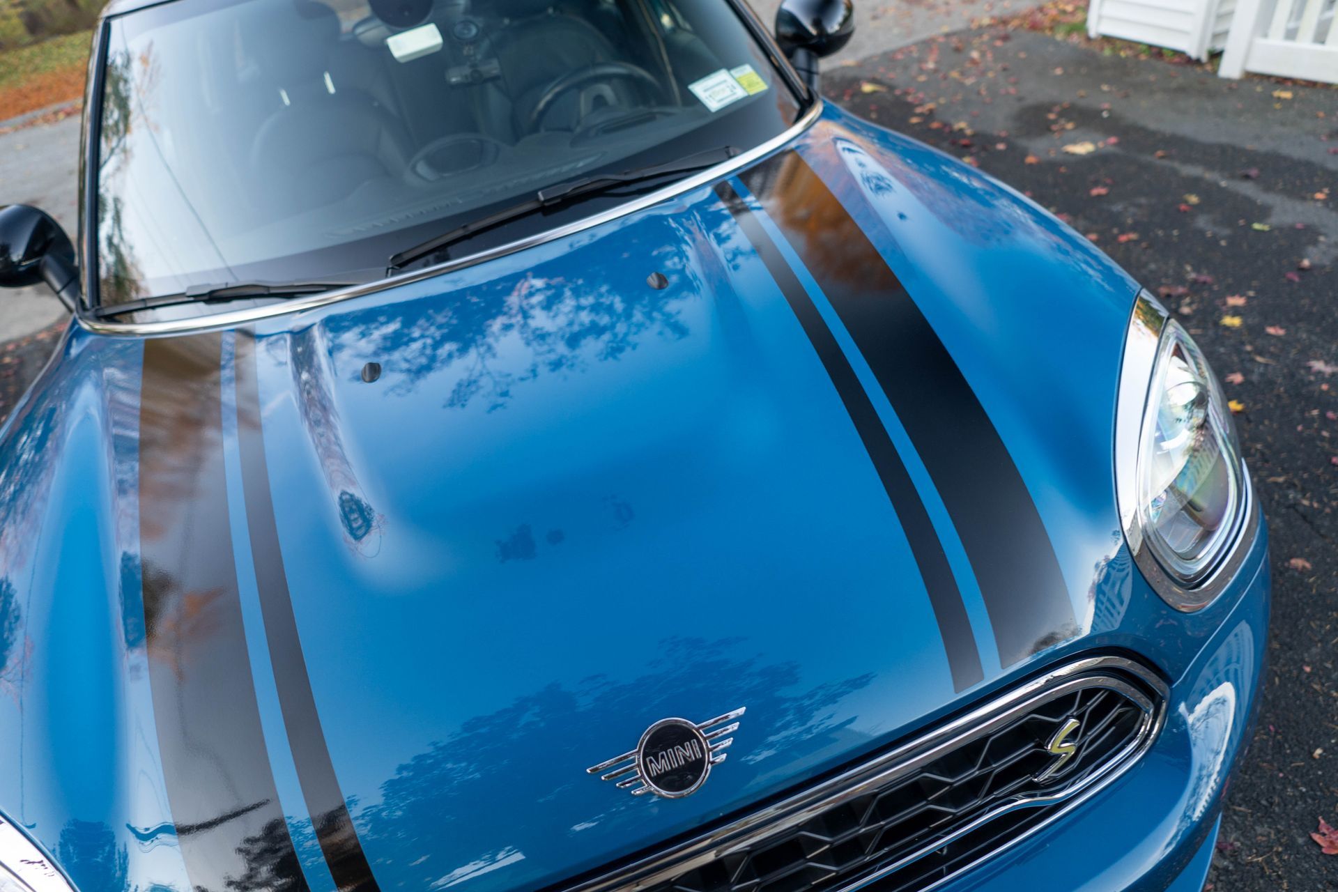 A blue mini cooper with black stripes on the hood