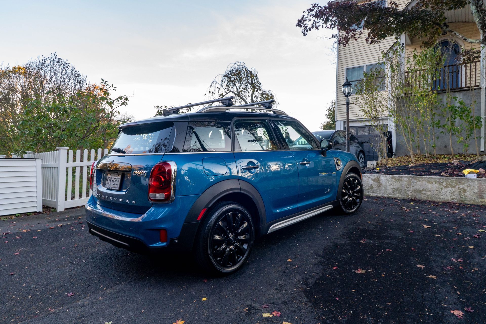 A blue mini cooper with a roof rack is parked in front of a house.