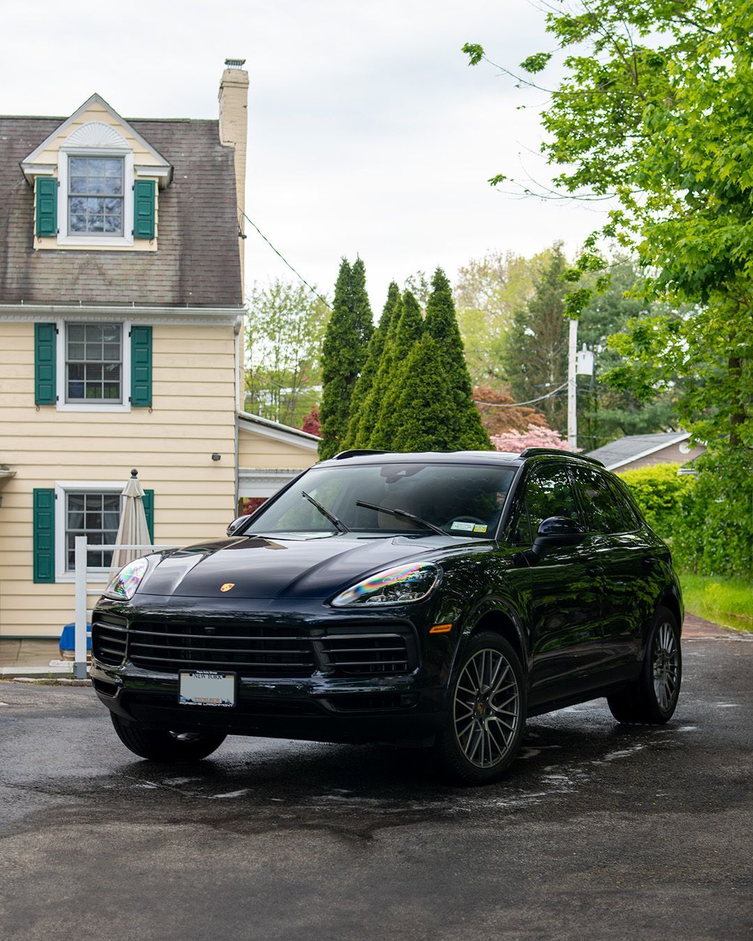 A black porsche cayenne is parked in front of a house.