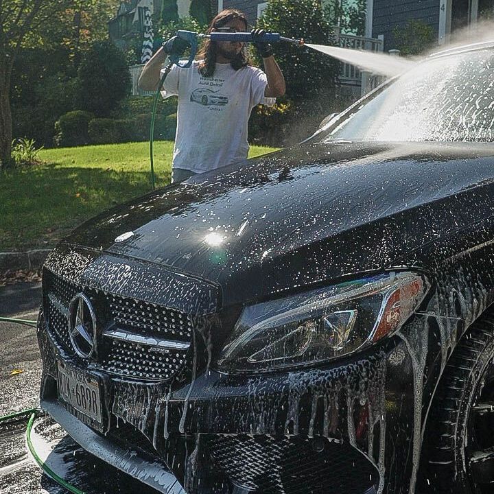 A man is washing a black mercedes with a high pressure washer