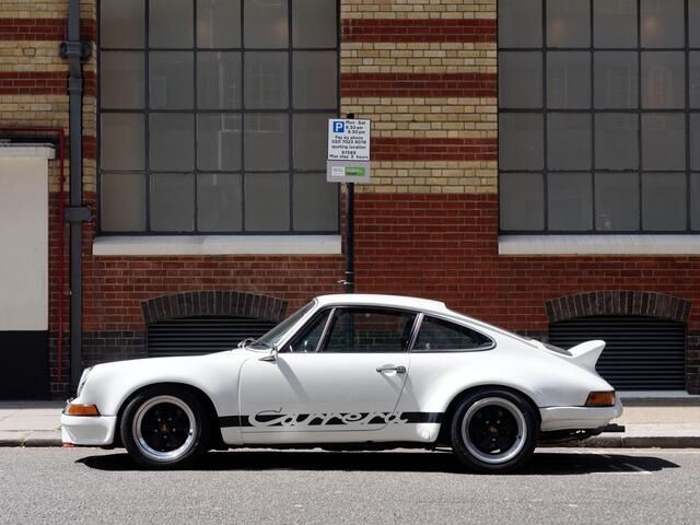 A white porsche is parked in front of a brick building.