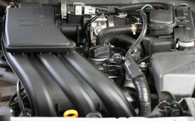 A close-up view of a modern car engine bay, showing black plastic intake manifolds, hoses, and mechanical components.
