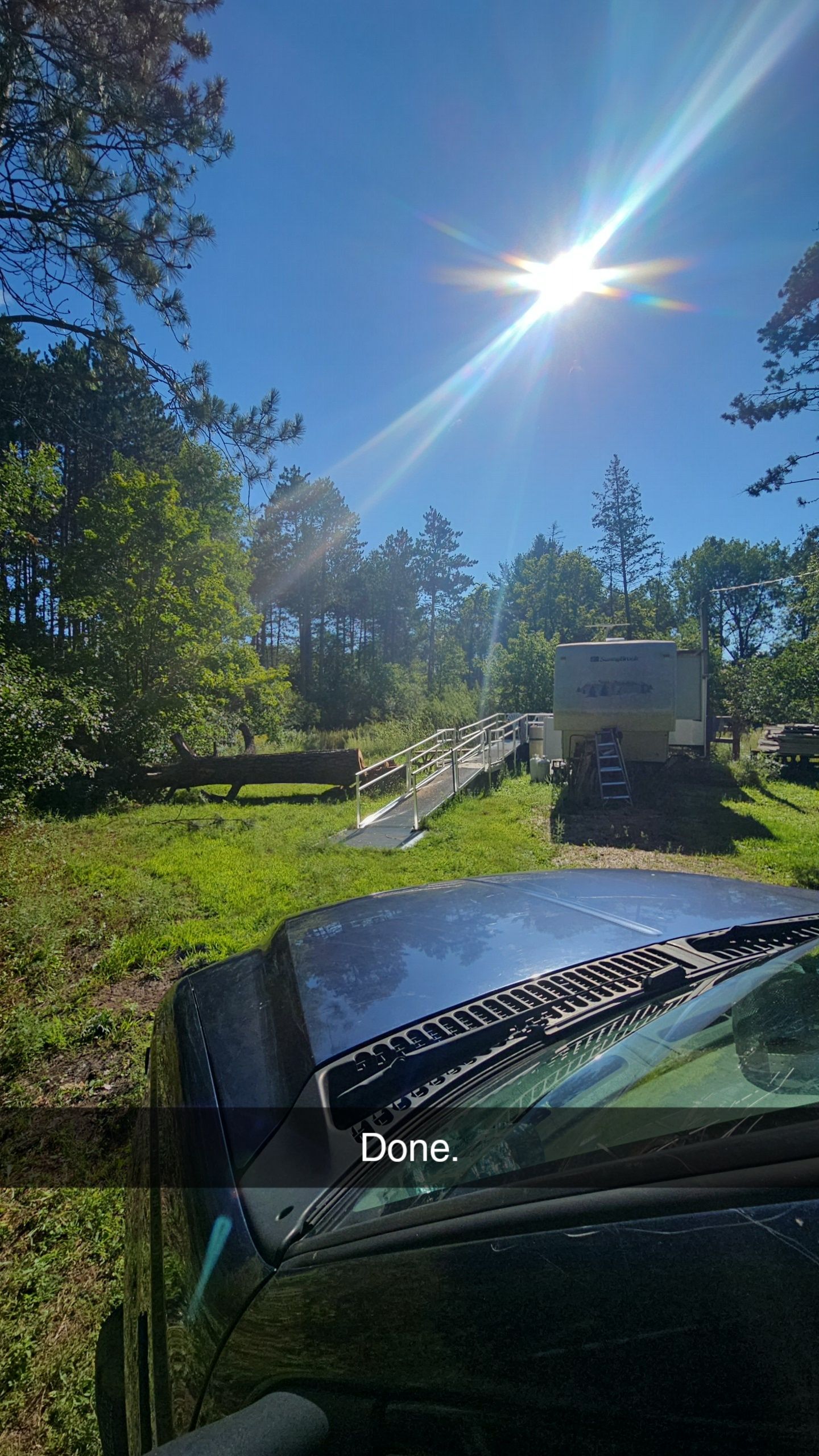 Bright sunny day, view from inside car looking at a wooded area with equipment and grass.