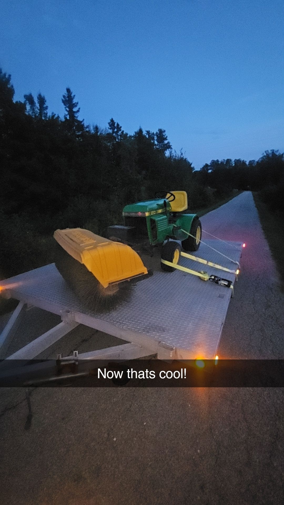 John Deere tractor and a yellow bucket on a flatbed trailer at dusk.