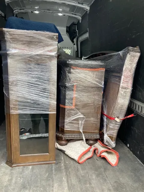 A van filled with furniture wrapped in plastic is being loaded.