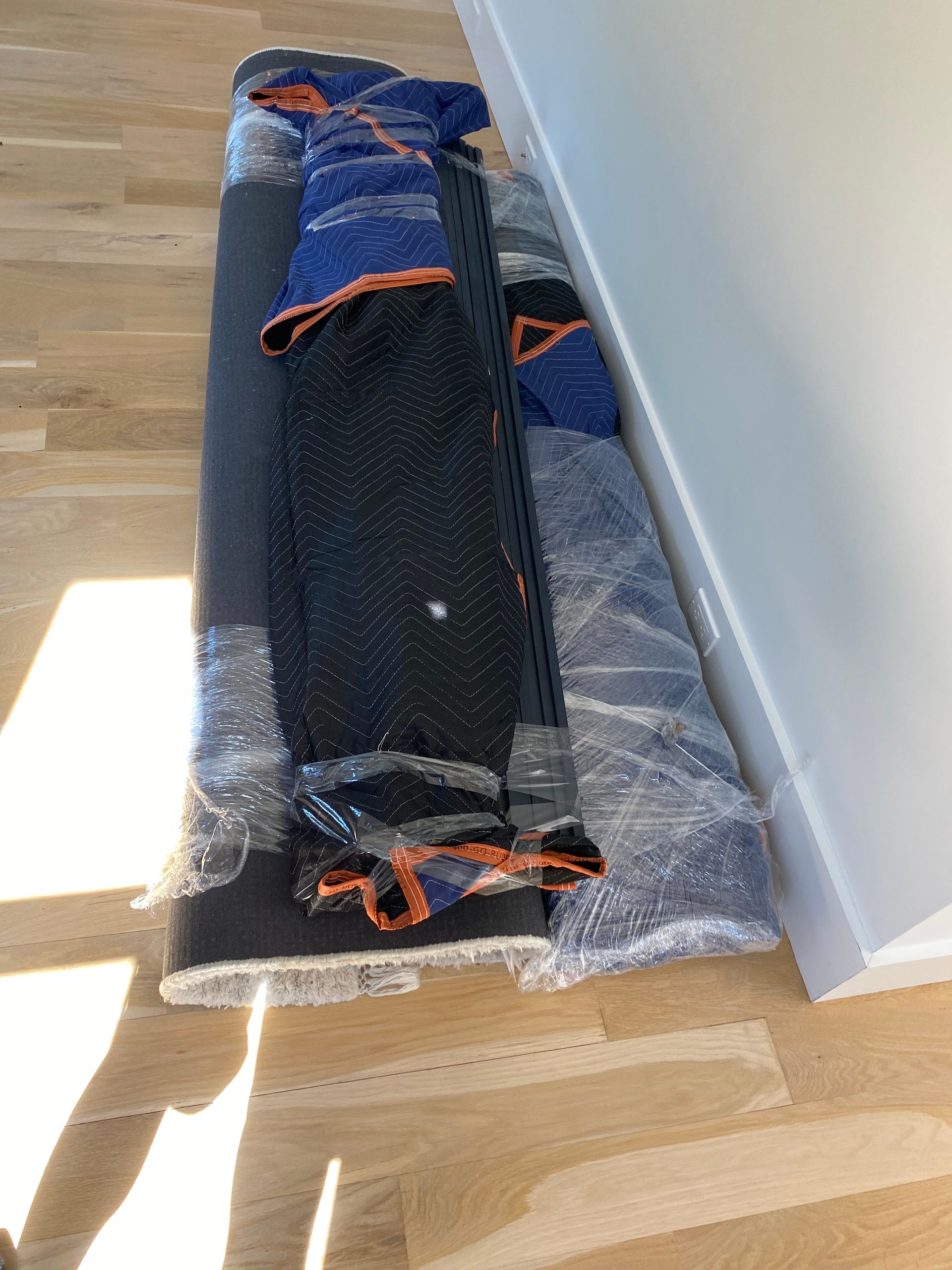 A skateboard is wrapped in plastic and sitting on a wooden floor.