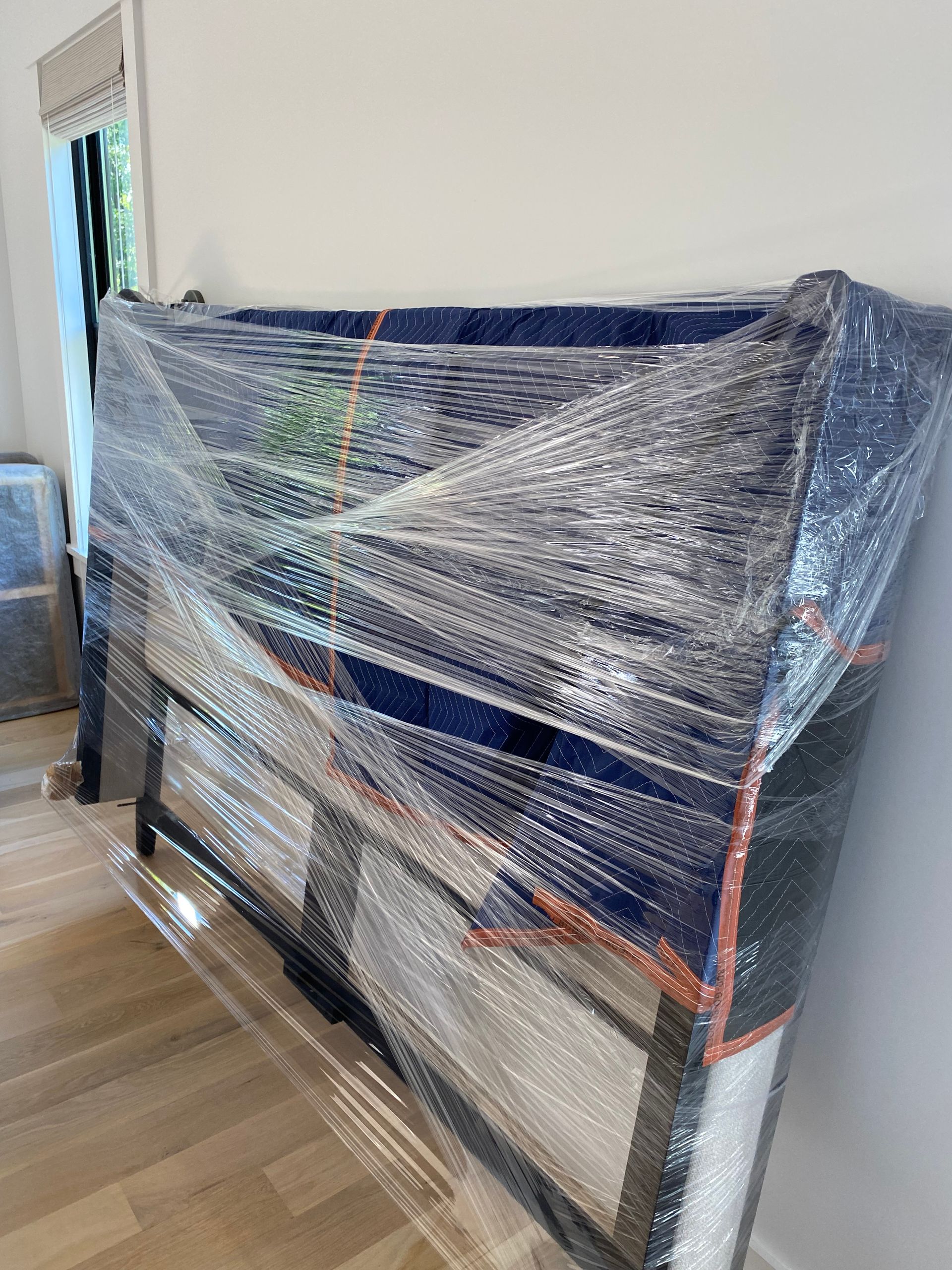 A piano is wrapped in plastic wrap in a living room.