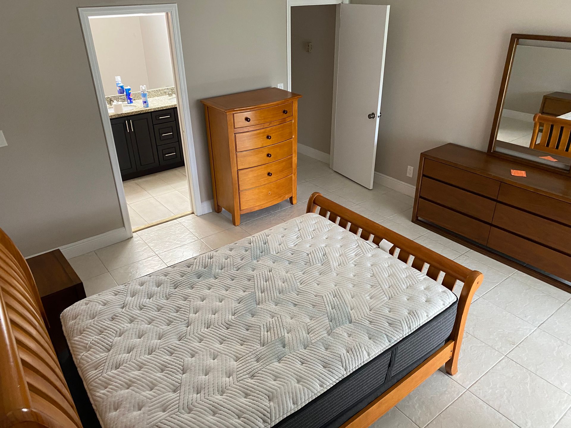 A bedroom with a bed , dresser , mirror and nightstand.