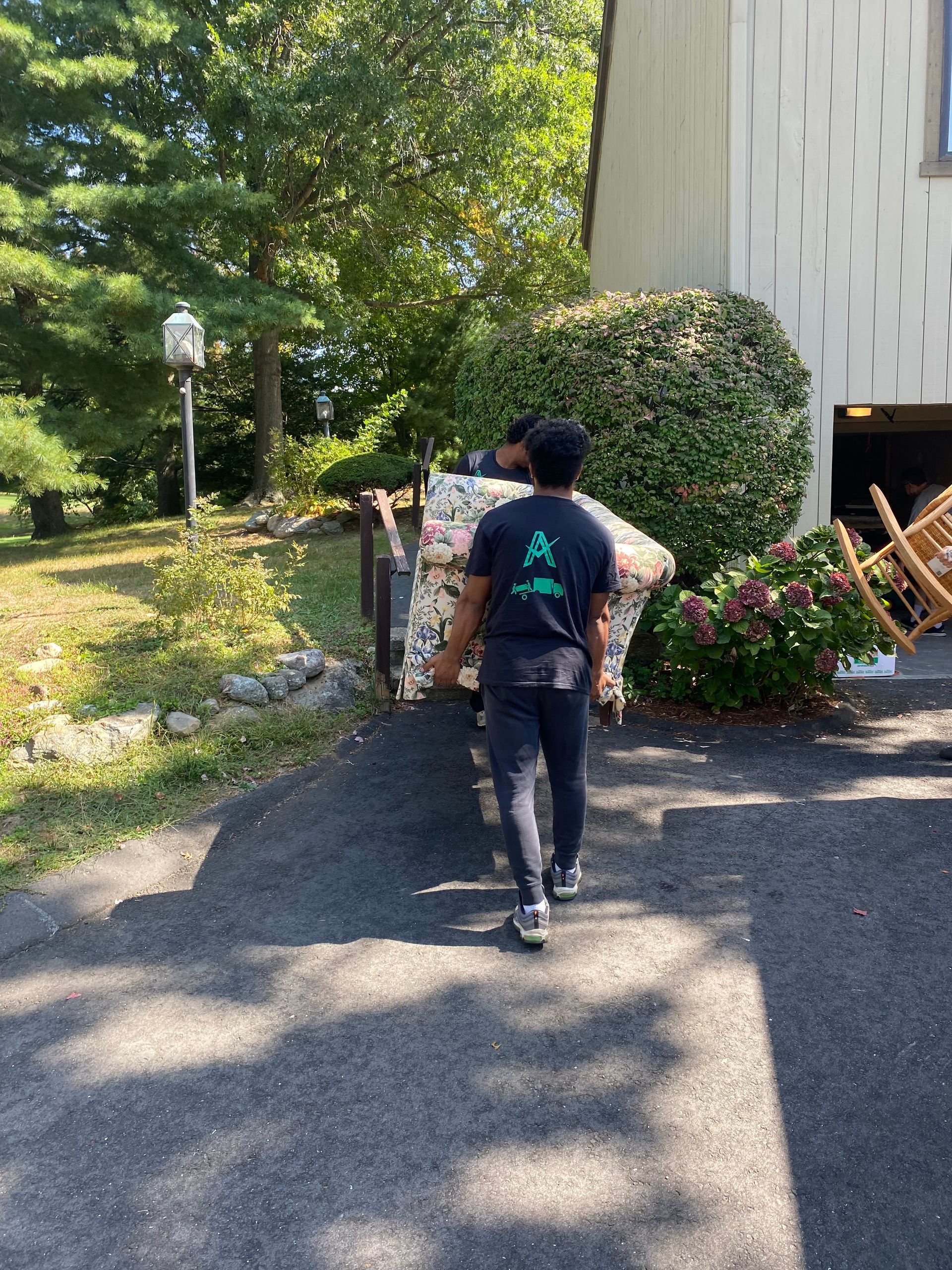 A man is carrying a large couch down a driveway.