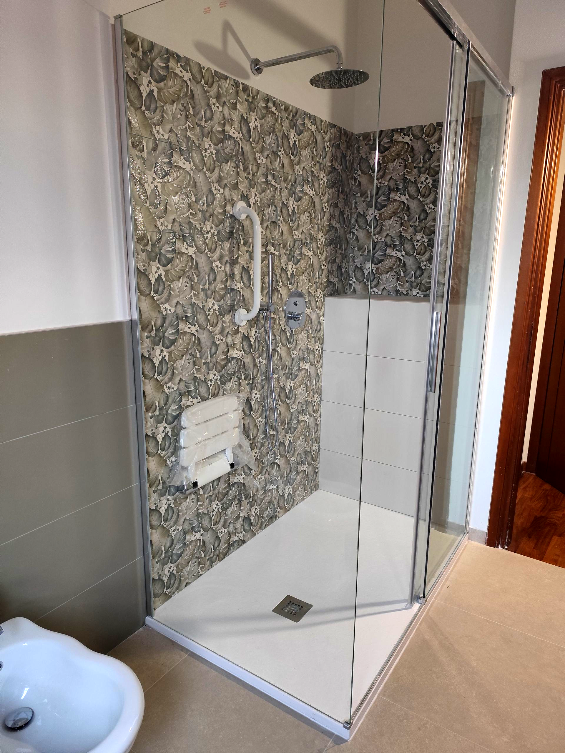 Bagno moderno con pareti in pietra grigio scuro, pavimento riflettente e specchio circolare con luci bianche.