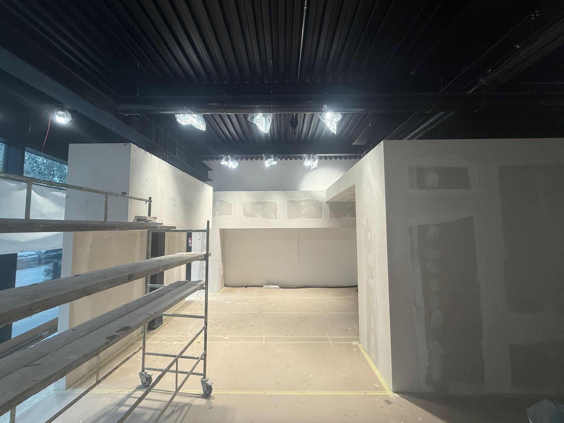 Costruzione di interni: pareti in cartongesso, soffitto nero, impalcature, luci sospese.
