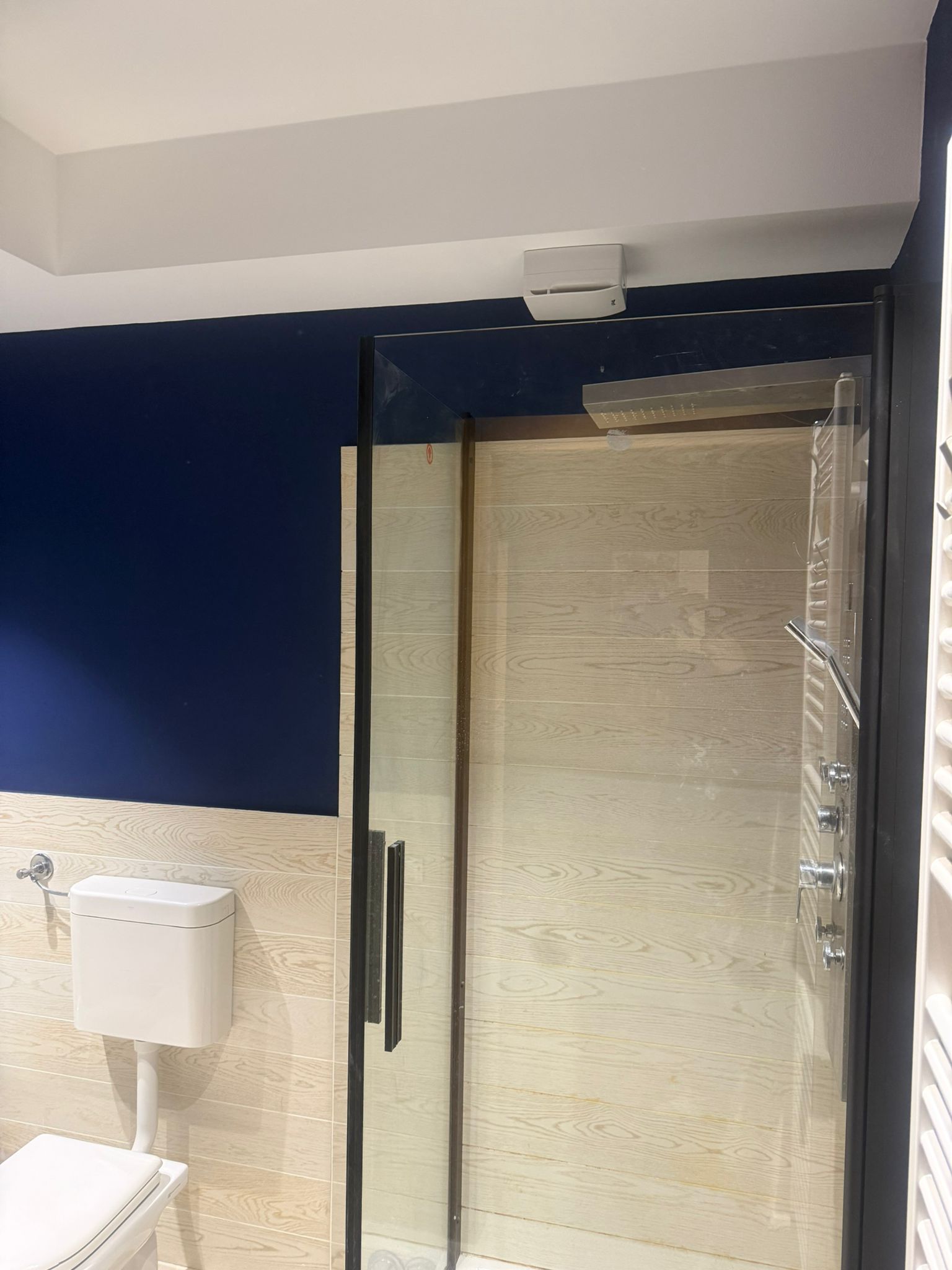 Bagno con porta doccia in vetro, parete blu e pareti piastrellate beige.