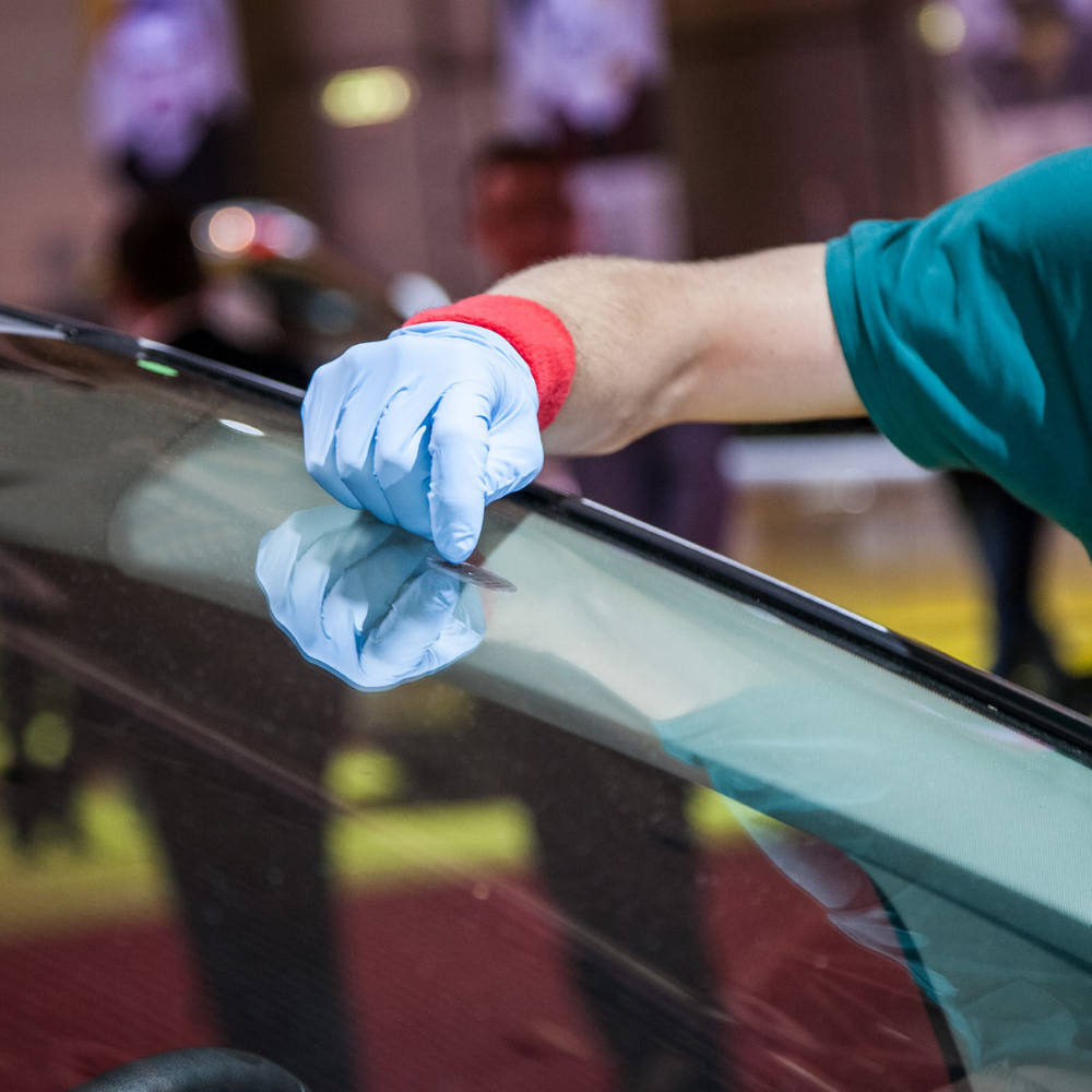 A person wearing blue gloves is cleaning the windshield of a car
