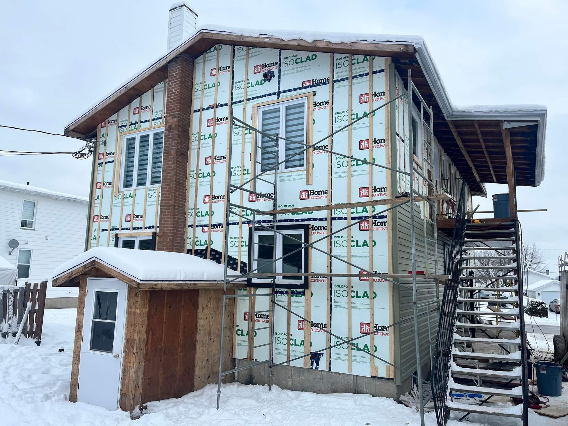 Une maison est en construction dans la neige, entourée d'échafaudages.