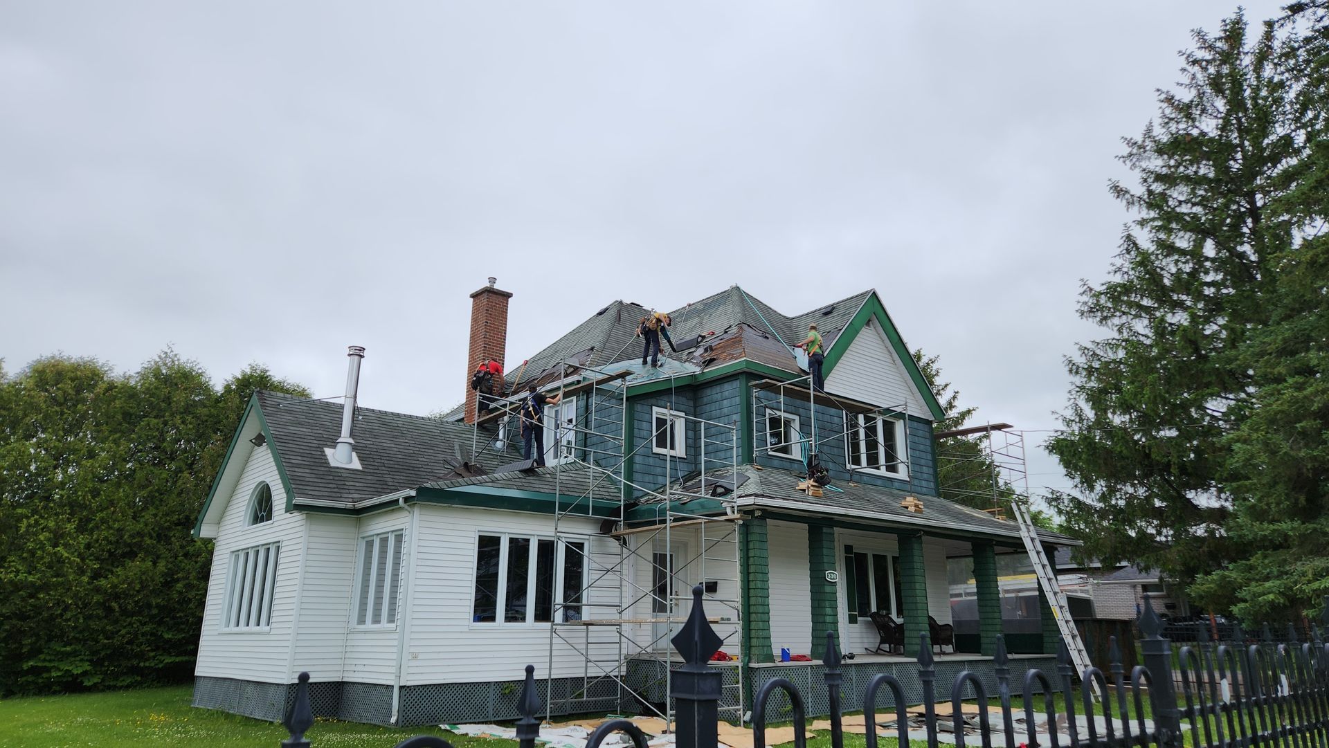 Une grande maison blanche avec une bordure verte est en train d'être repeinte.