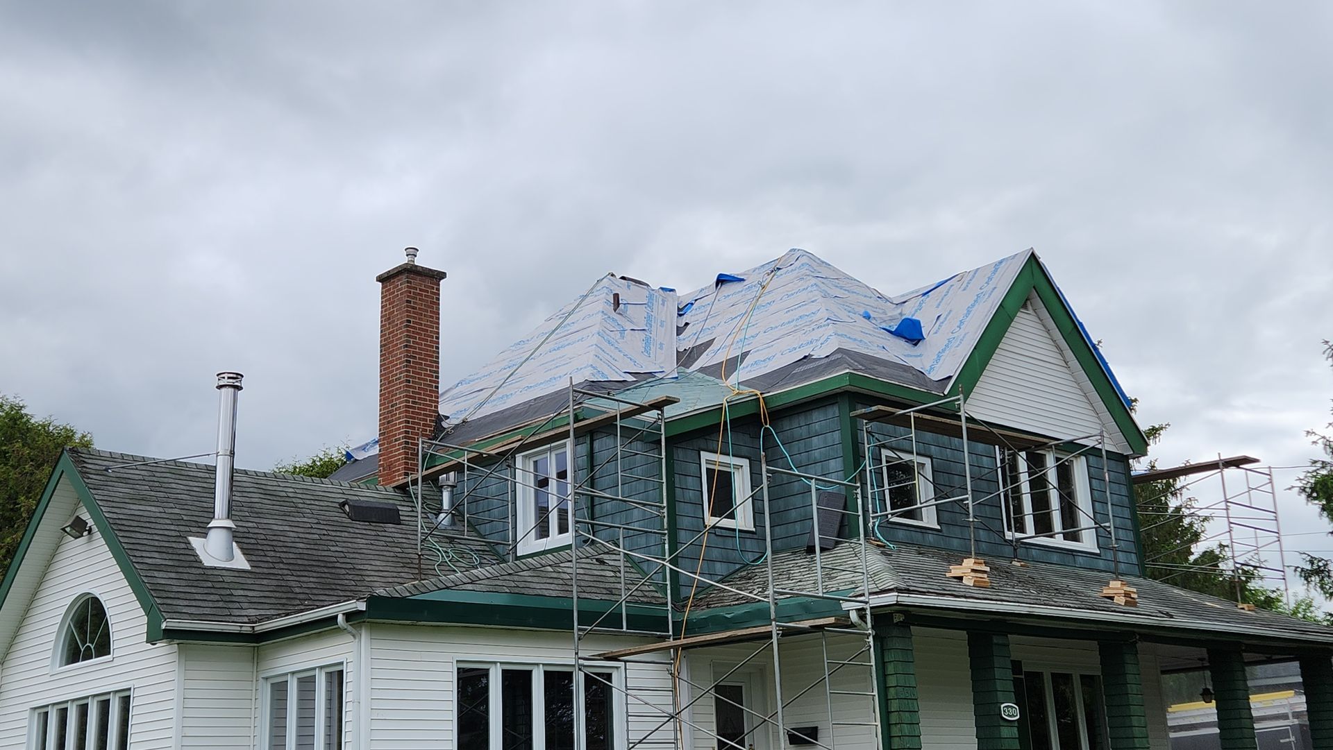 Une grande maison blanche avec une bordure verte est en cours de rénovation.