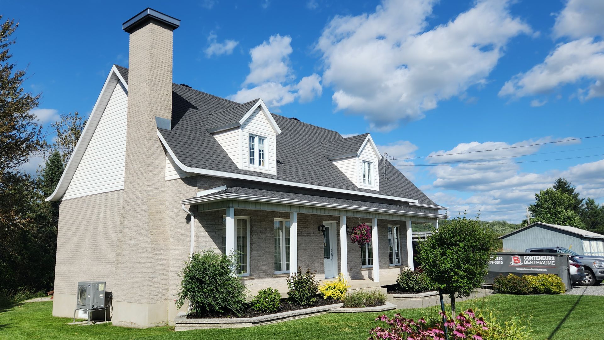 Une grande maison avec un porche et une cheminée par une journée ensoleillée.