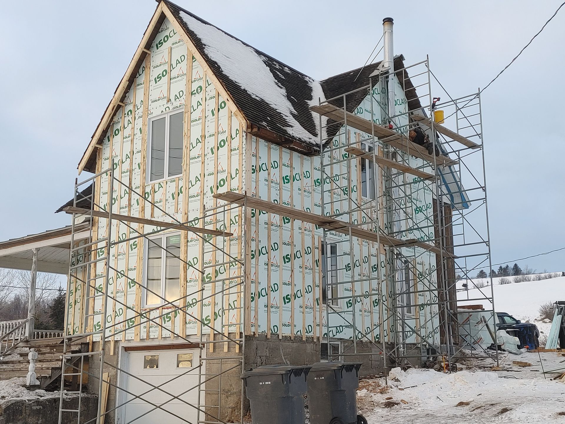Une maison est en construction dans la neige, entourée d'échafaudages.