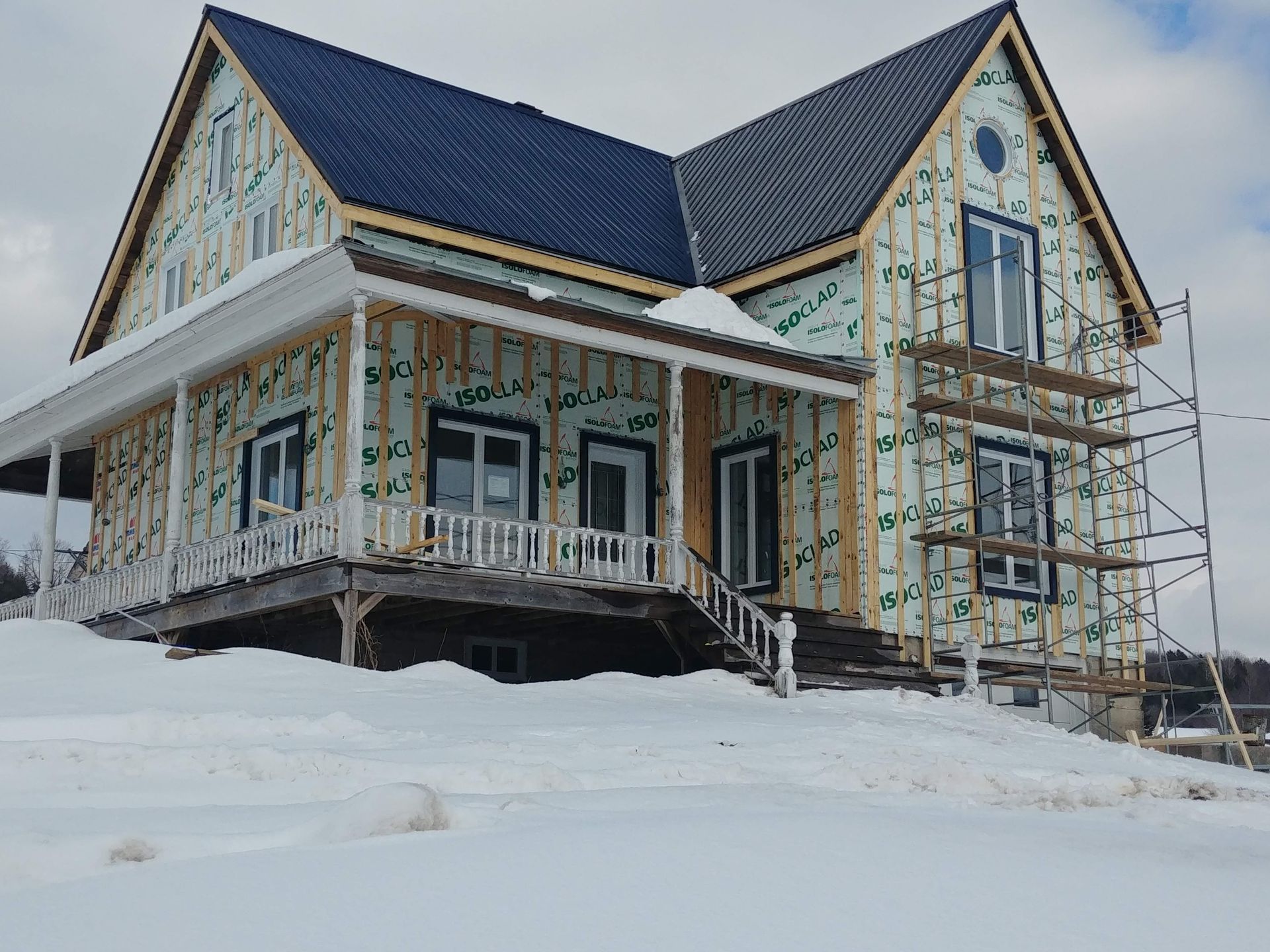 Une maison est en construction dans la neige, entourée d'échafaudages.